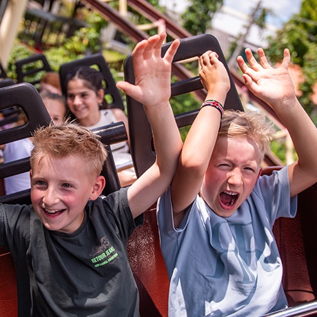 2 Kinder in der Achterbahn mit hochgerissenen Armen.